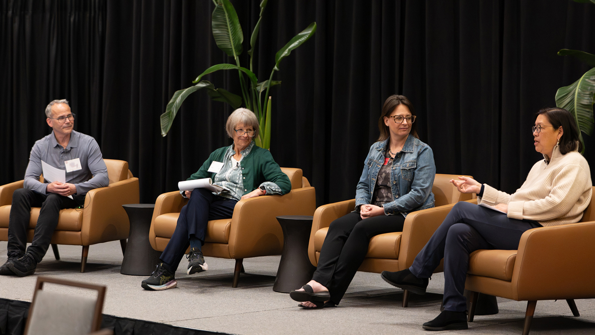 a panel of speakers in chairs on a stage