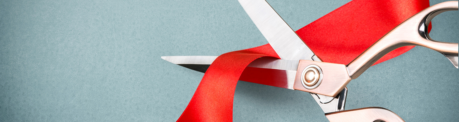 Scissors cutting red ribbon, close-up view on blue background