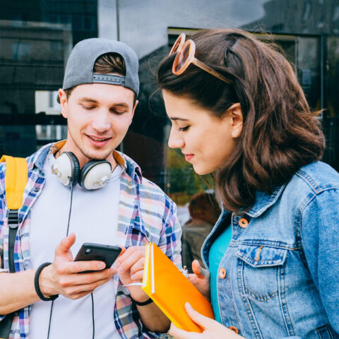 two students waiting for a bus check schedules on their phone